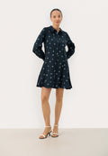 Navyblaues Hemdkleid mit langen Ärmeln, Knopfverschluss und weißen Blumenmustern. Ausgestellt geschnitten, aus einem glatten Stoff gefertigt, kombiniert mit nudefarbenen Absätzen.