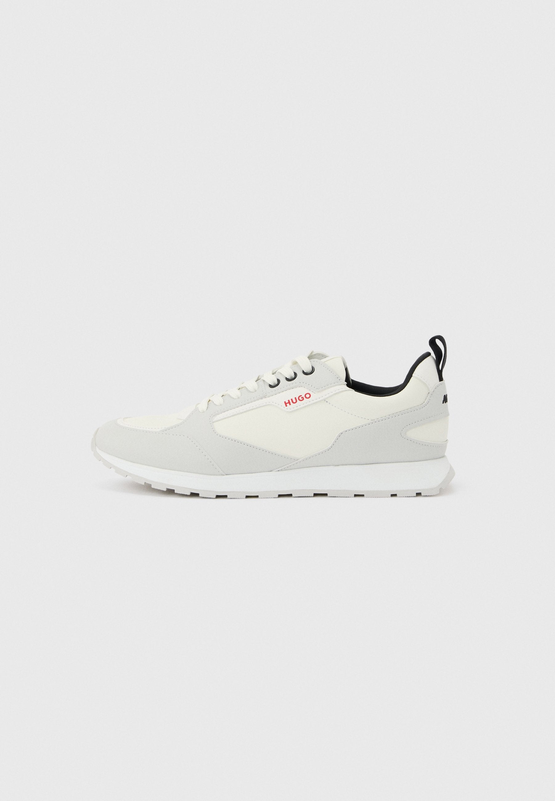 Niedrig geschnittener weißer und hellgrauer Sneaker mit weißer Sohle, Schnürverschluss, schwarzem Zuglasche und kleinem roten "HUGO"-Logo an der Seite.