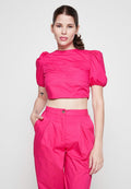 Fuchsia Cropped-Top mit Puffärmeln und strukturiertem Design, kombiniert mit hoch taillierten, gefältelten Fuchsia-Hosen, alles aus glattem Stoff.