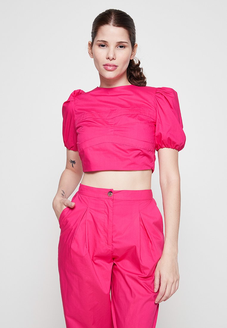 Fuchsia Cropped-Top mit Puffärmeln und strukturiertem Design, kombiniert mit hoch taillierten, gefältelten Fuchsia-Hosen, alles aus glattem Stoff.