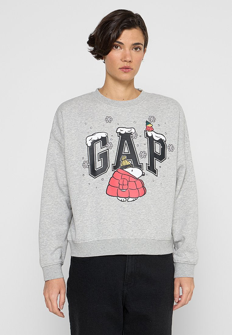 Junge Person trägt ein graues Sweatshirt mit den Buchstaben "GAP", bedeckt mit Schnee und einer Illustration eines Eisbären in roter Jacke und gelbem Hut.