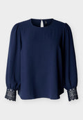 Marineblaue langärmlige Bluse mit Spitzenmanschetten, Puffärmeln, rundem Ausschnitt und einem kleinen Knopfverschluss hinten.