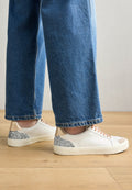 Weiße Leder-Sneaker mit braunen Akzenten und silbernem Glitzer auf der Ferse, mit einer runden Zehenpartie und flachen Sohlen, kombiniert mit blauen Denim.