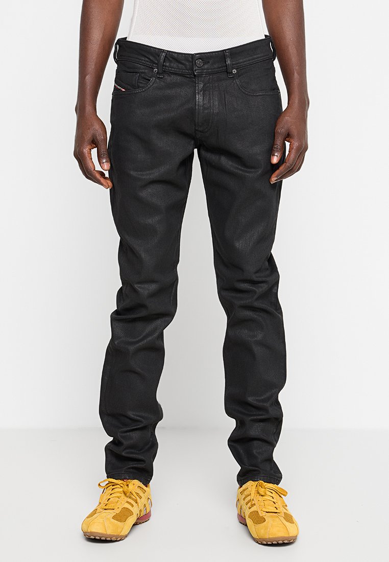 Schwarze Denim-Jeans mit slim fit, mit einem Fünf-Taschen-Design, betonten Nähten und einer glatten Textur. Kombiniert mit gelben Sportschuhen.