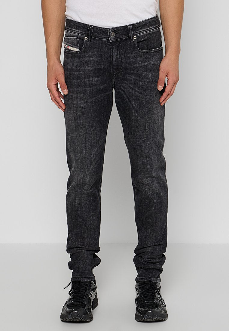 Dunkelblaue Denim-Jeans mit einer schlanken Passform, die fünf Taschen und subtile Waschungen aufweisen. Der Stoff hat eine glatte Textur mit leichten Verfärbungen.