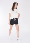 Weißes Baumwoll-T-Shirt mit einem grünen Herz-Symbol, kombiniert mit schwarzen Baumwollshorts mit einer weißen Schnur. Getragen mit weißen Sneakers.
