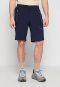 Mann trägt marineblaue Shorts mit Reißverschluss, beige Socken und graue Sneakers mit blauen Schnürsenkeln und steht vor einfachem Hintergrund.
