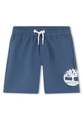 Marineblaue Badeshorts mit elastischem Bund und weißem Kordelzug; mit einem weißen Baumlogo am linken Bein und seitlichen Taschen.