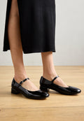 Schwarze Lackleder-Mary-Jane-Schuhe mit kleinem Blockabsatz, ausgestattet mit einem Riemen über dem Spann und einem abgerundeten Zehendesign. Glatte Textur.