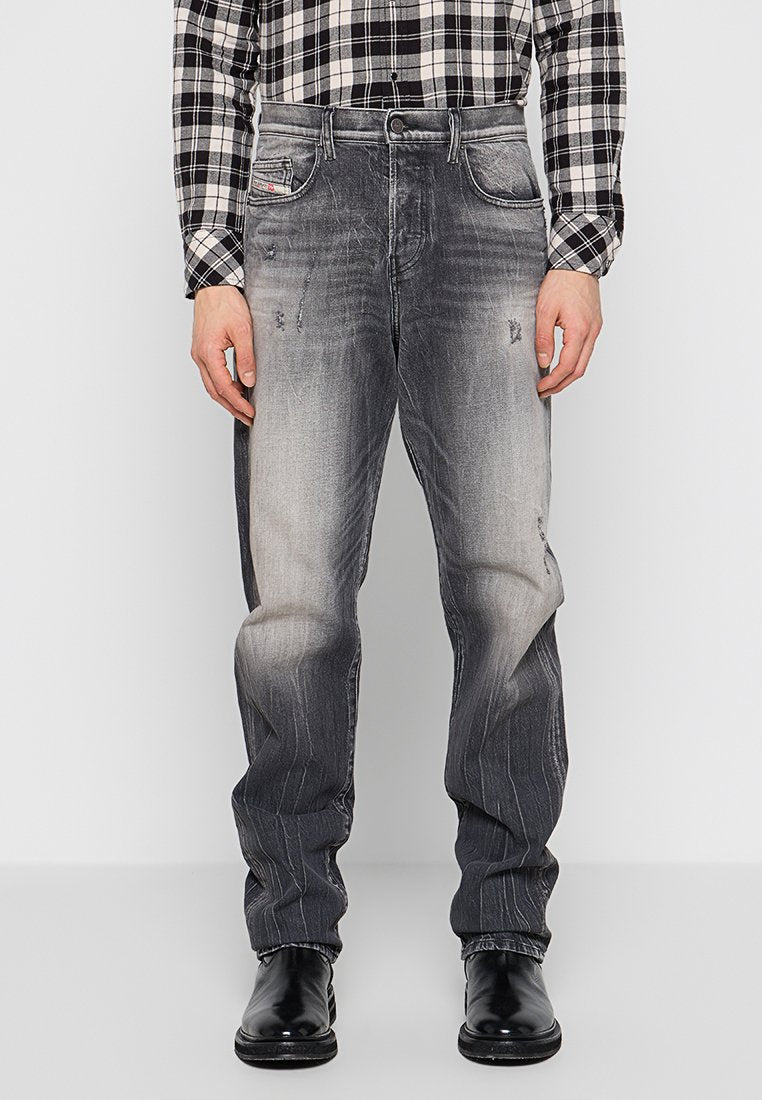 Graue Denim-Jeans mit einem ausgebleichten Finish, im entspannten Schnitt, mit dezentem Verblassen und abgenutzten Details. Getragen mit schwarzen Schuhen.