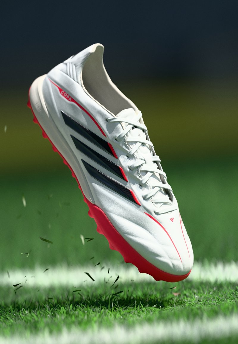 Weißer Fußballschuh mit roten Akzenten und schwarzen Streifen. Verfügt über eine glatte Oberfläche, Schnürdesign und eine strukturierte Sohle für besseren Halt.