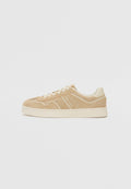 Beige Wildlederschuhe mit einem niedrigen Design, ausgestattet mit cremefarbenen Akzenten und einer strukturierten Sohle. Dezente Nähdetails und Logo an der Seite.