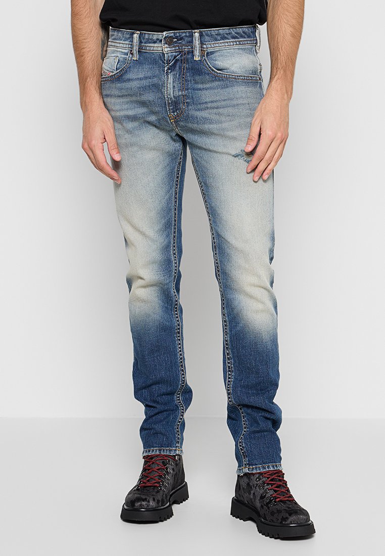 Hellblaue Jeans mit einem verblassten Verlauf, regulärer Schnitt, fünf Taschen und kontrastierenden Nähten. Kombiniert mit schwarzen Stiefeln mit roten Schnürsenkeln.