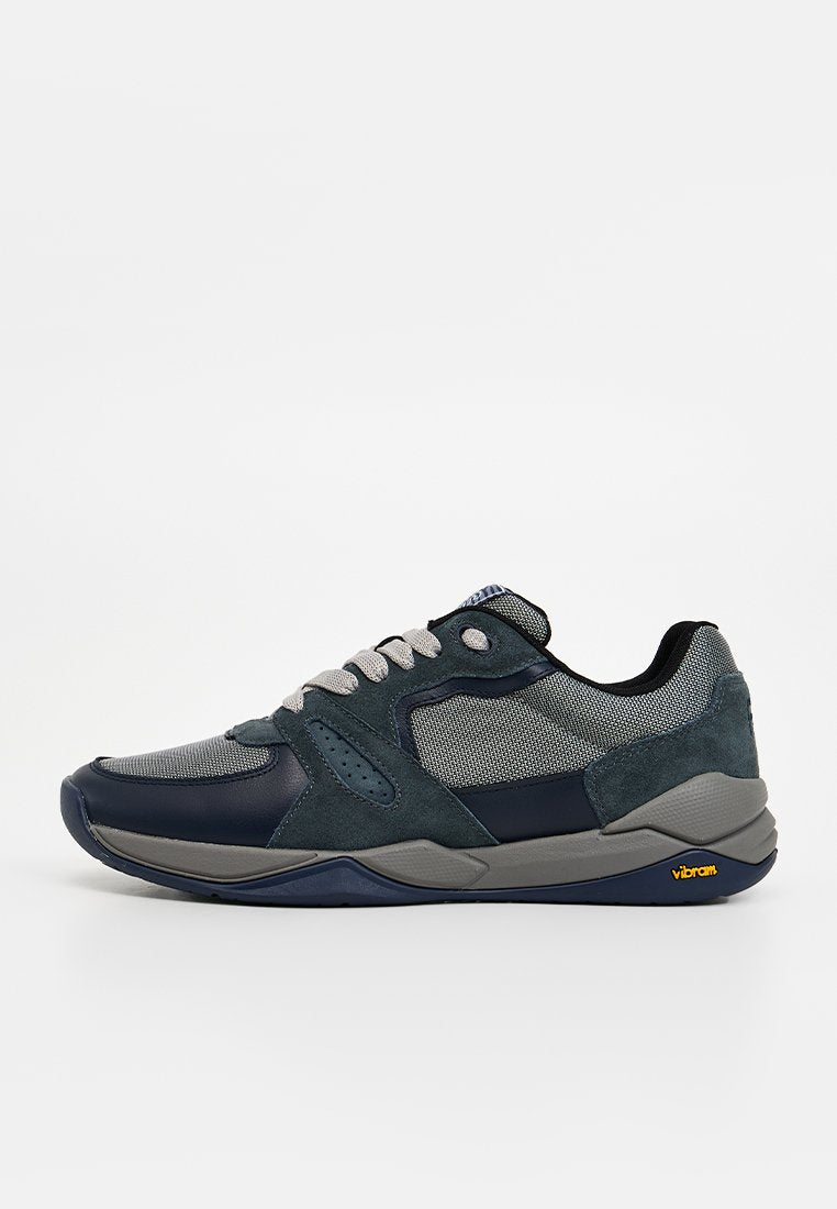 Sneakers mit einer Mischung aus marineblauen und grauen Materialien, bestehend aus Mesh, Wildleder und Gummisohle, akzentuiert mit einem gelben Vibram-Logo.