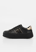 Schwarzer Sneaker mit niedrigem Schaft, dicker Sohle, goldenem Fersenakzent, schwarzen Schnürsenkeln und kleinem goldenen Schnallendetail an der Seite.