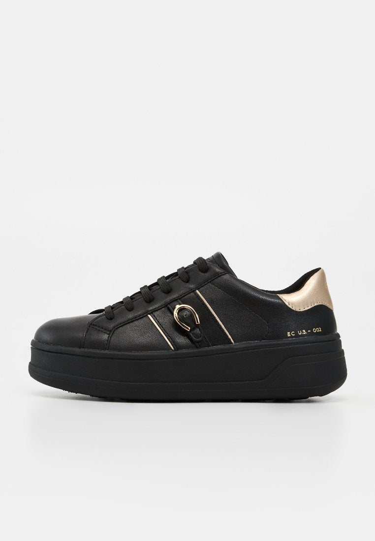 Schwarzer Sneaker mit niedrigem Schaft, dicker Sohle, goldenem Fersenakzent, schwarzen Schnürsenkeln und kleinem goldenen Schnallendetail an der Seite.