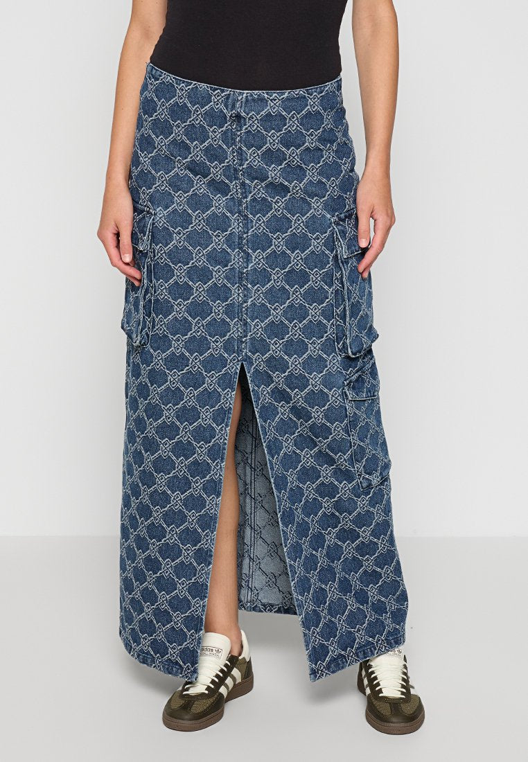 Jeans-Maxi-Rock mit geometrischem Muster, ausgestattet mit einem Schlitz vorne, zwei seitlichen Taschen und einem taillierten Bund, getragen mit Sneakers.