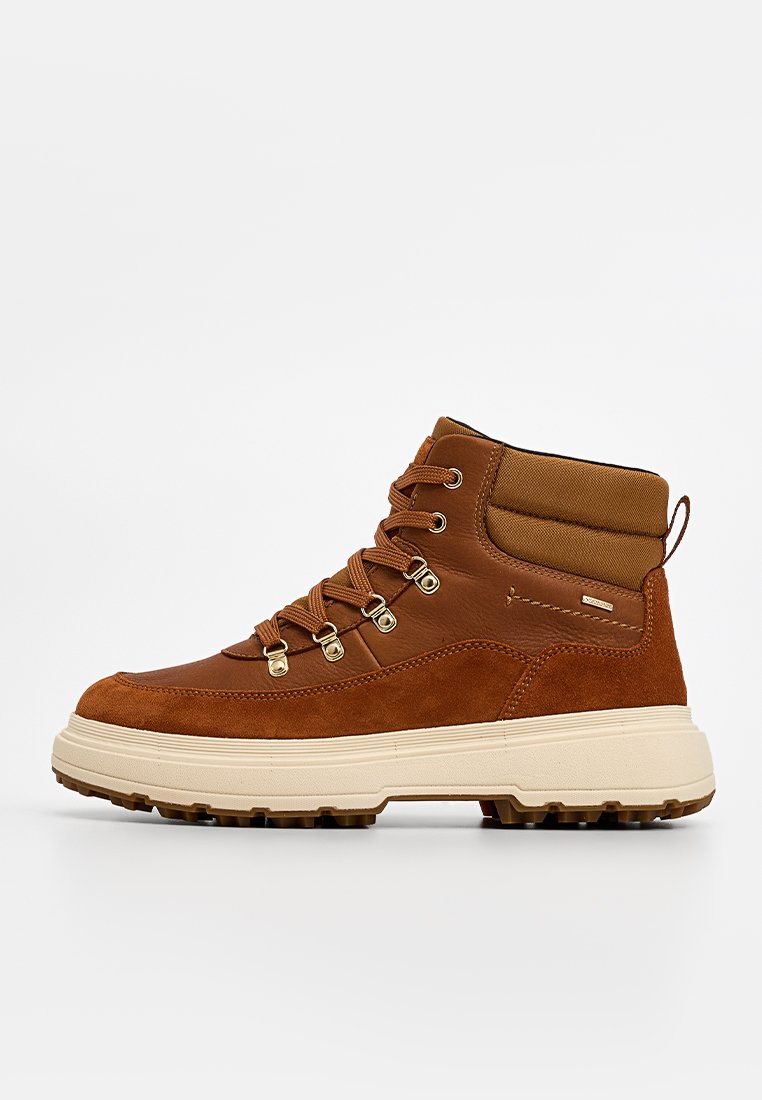 Brauner Wanderschuh aus einer Mischung von Wildleder und Leder, mit hohem Knöcheldesign, Metallösen und einer dicken beigefarbenen Gummisohle.