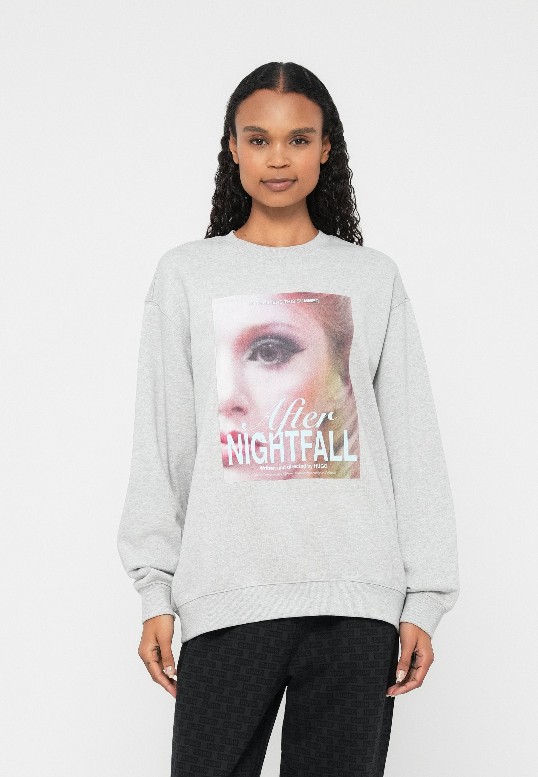 Grauer Pullover mit langen Ärmeln, mit großem grafischem Druck eines Gesichts und dem Text "After NIGHTFALL." Weiche Textur und lockere Passform.