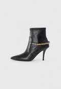 Schwarzer Lederknöchelstiefel mit spitzem Zeh, hohem Stiletto-Absatz und dekorativem gold- und silberfarbenem Kettenakzent um den Knöchel.