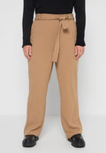 Helle beigefarbene Hochbundhose mit einem Stoffgürtel, weit geschnitten, und einer glatten Textur, kombiniert mit einem schwarzen, gerippten Langarmoberteil und klobigen schwarzen Schuhen.