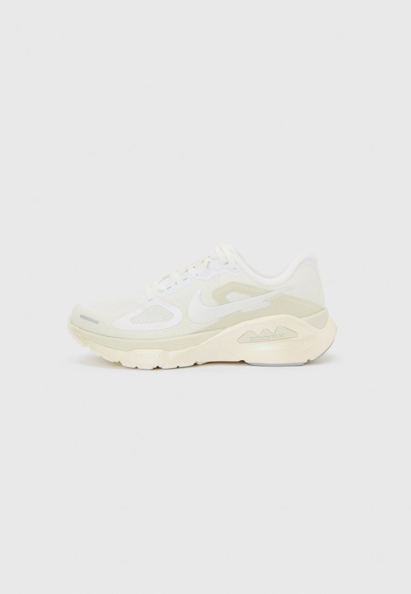 Beiger und weißer Nike-Laufschuh mit niedrigem Schaft, gepolsterter Sohle und Mesh-Einsätzen, von der Seite auf unifarbenem Hintergrund gezeigt.