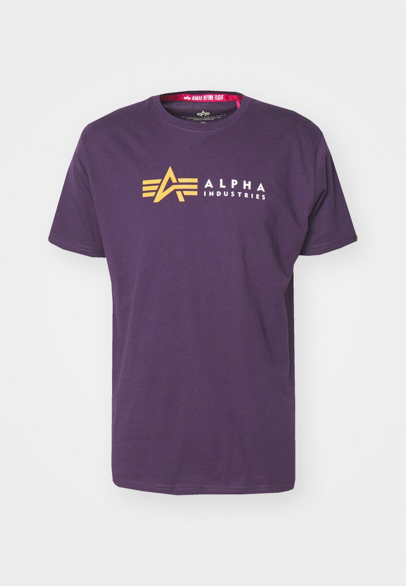 Lila Baumwoll-T-Shirt mit einem gelben "A"-Logo und dem Text "ALPHA INDUSTRIES" in Weiß. Mit kurzen Ärmeln und rundem Halsausschnitt.