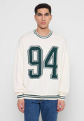 Weißer Pullover aus Strick mit grünen Akzenten, der die Zahl "94" auffällig auf der Vorderseite trägt. Rippstrickkragen und -bündchen.