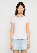 Weißes geripptes T-Shirt mit kurzen Ärmeln und Rundhalsausschnitt, versehen mit dekorativen Stickdetails über der Brust, kombiniert mit einem hellen Jeansrock.