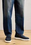 Marineblaue Wildleder-Slipper mit weißer Gummisohle, kombiniert mit verwaschenen blauen Jeans im geraden Schnitt. Die Schuhe verfügen über einen einfachen gestickten Akzent.
