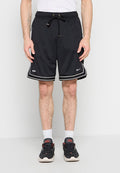 Mann trägt schwarze Nike-Basketballshorts mit weißem Rand, weiße Socken und schwarze Sportschuhe, steht vor einem schlichten Hintergrund.
