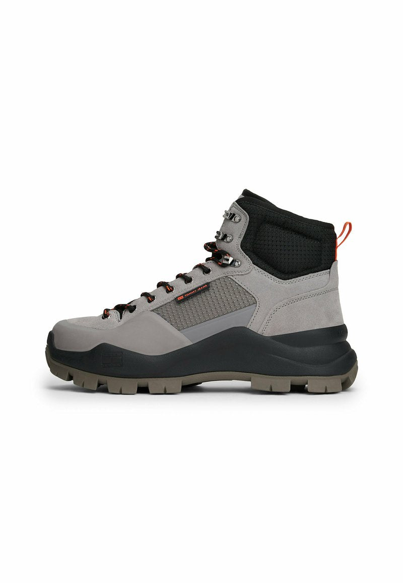 Wanderstiefel mit hohem Schaft aus grauem Wildleder und Mesh, ausgestattet mit einem schwarzen, gepolsterten Kragen, orangefarbenen Akzenten und einer robusten schwarzen Gummisohle mit Profilstollen.