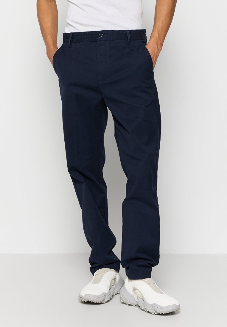 Navy Baumwoll-Chinos mit geradem Bein, Knopfverschluss und Seitentaschen, kombiniert mit hellen Sneakers.