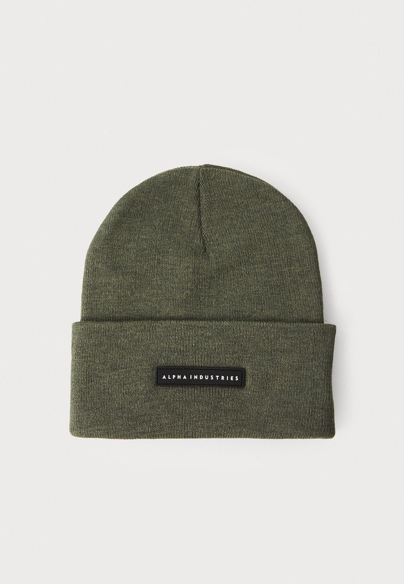Olivgrüner Strickbeanie mit Umschlag, ausgestattet mit einem rechteckigen schwarzen Etikett, auf dem "ALPHA INDUSTRIES" in weißem Text steht. Weiche Textur.