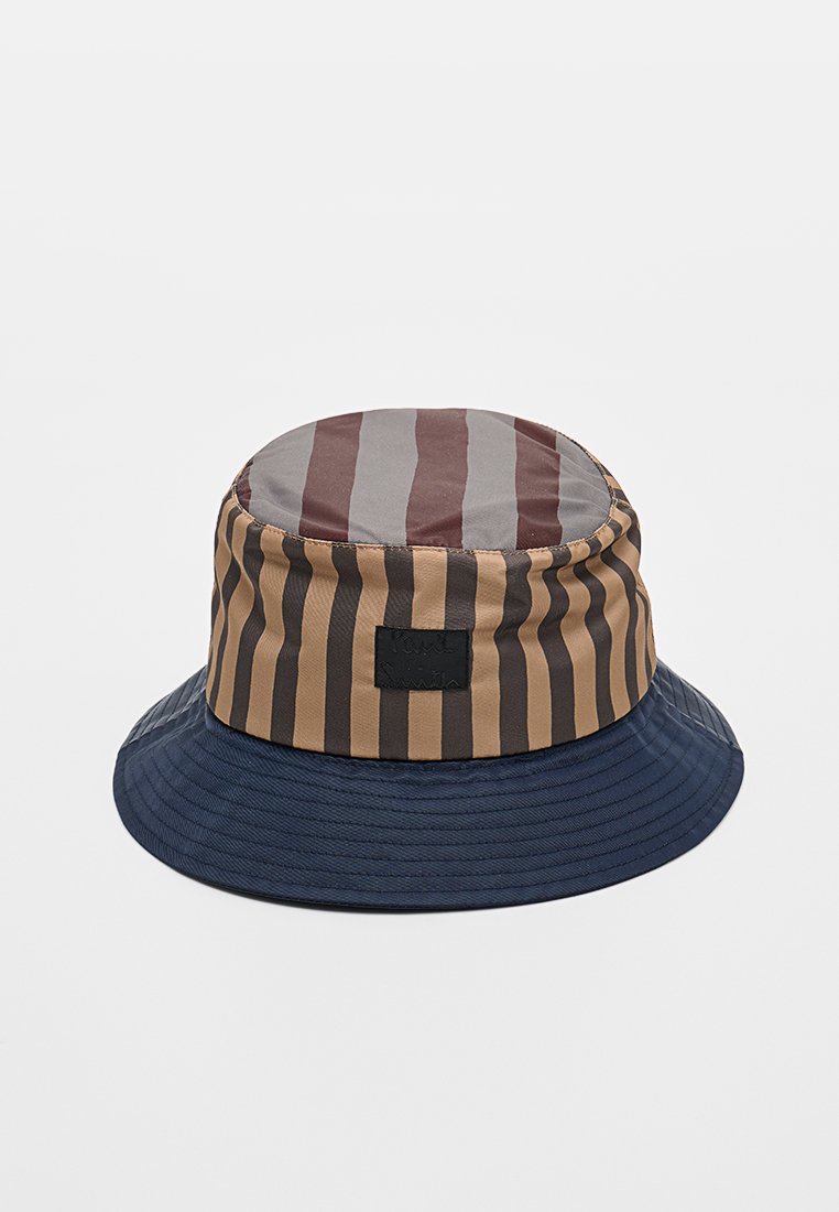 Bucket Hat mit breiter marineblauer Krempe und braunen, beigen und grauen vertikalen Streifen auf der Krone, mit rechteckigem schwarzem Patch vorn.