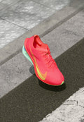Neon-pinke Laufschuhe mit einer strukturierten Oberseite, gelbem Swoosh-Logo und mintgrüner Sohle. Enthält Schnürsenkel und verstärkten Zehenbereich.