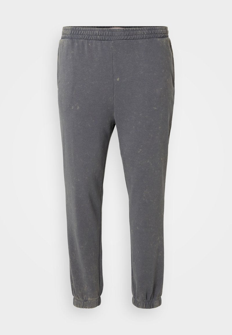 Graue, weiche Stoff-Jogginghosen mit elastischem Bund. Schmal zulaufende Beine und gesäumte Säume, die eine subtile, abgenutzte Textur aufweisen.