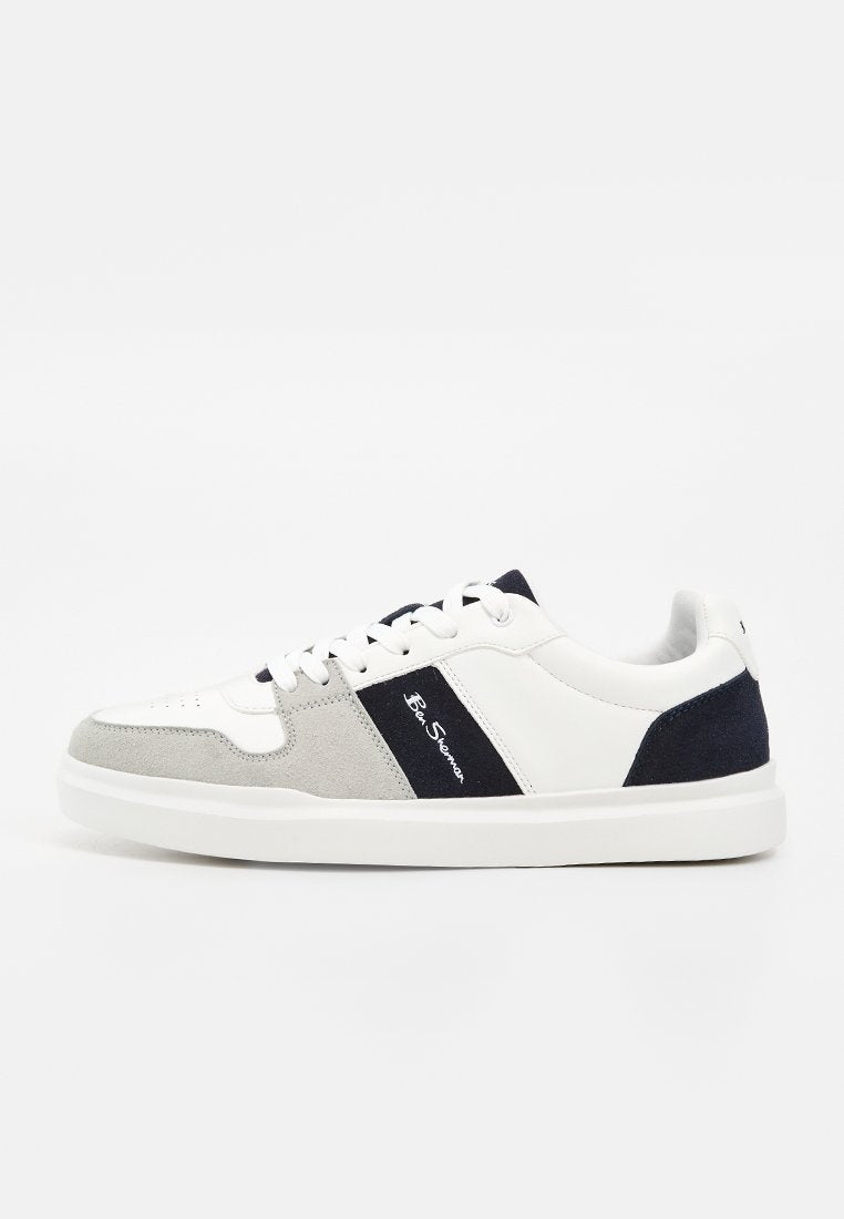 Weißer Sneaker mit niedrigem Schaft, grauen und marineblauen Wildlederakzenten, weißen Schnürsenkeln und einem schwarzen Seitenstreifen mit kleinem weißen Text.