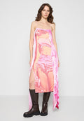 Rosa grafisches Kleid mit dünnen Trägern, versehen mit einem übergroßen Fotodesign. Text auf dem Stoff und seitlichen Schlitzen. Kombiniert mit knielangen braunen Stiefeln.