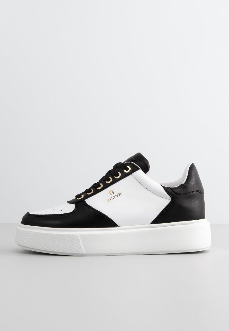 Schwarze und weiße Low-Top-Sneaker mit dicker weißer Sohle, schwarzen Schnürsenkeln, goldenen Ösen und "Aigner"-Logo auf der Seitenfläche.