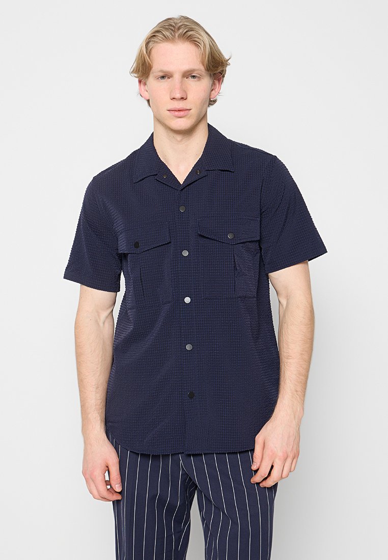 Marineblaues Kurzarmhemd mit strukturiertem Muster, mit durchgehender Knopfleiste und zwei Brusttaschen. Hergestellt aus leichtem, atmungsaktivem Stoff.