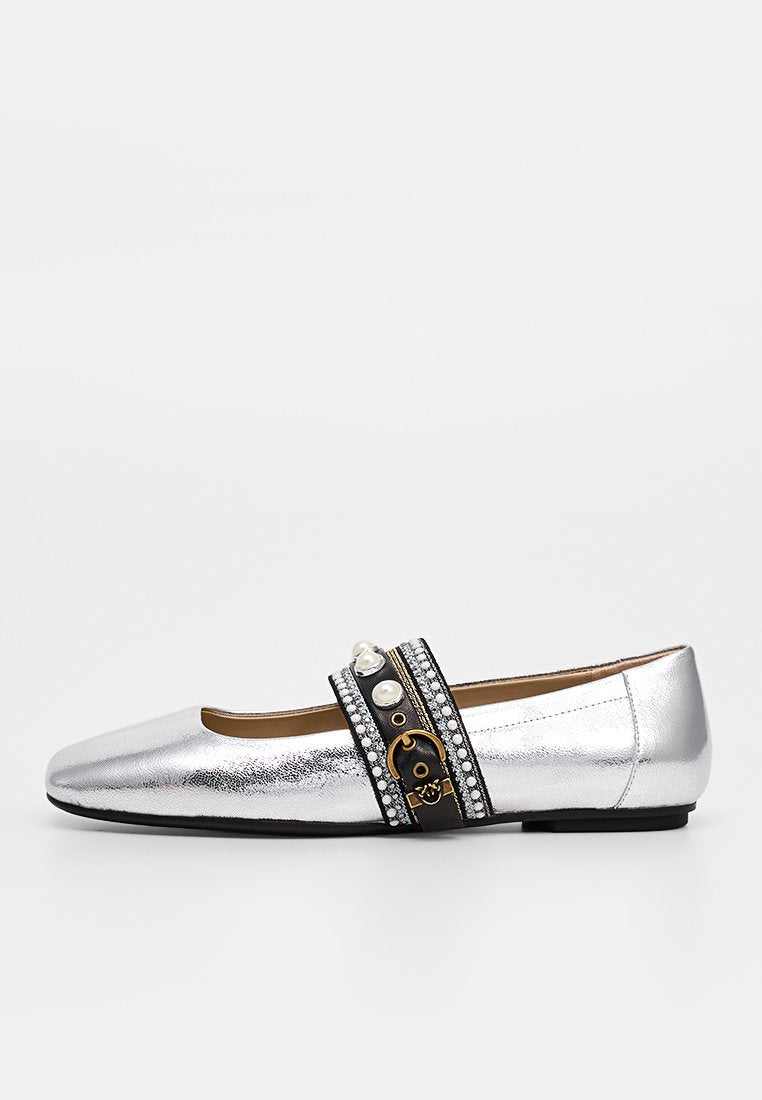 Silberner flacher Schuh mit schwarzem Riemen, verziert mit Perlen, Strasssteinen und einer kleinen goldenen Schnalle, vor weißem Hintergrund.
