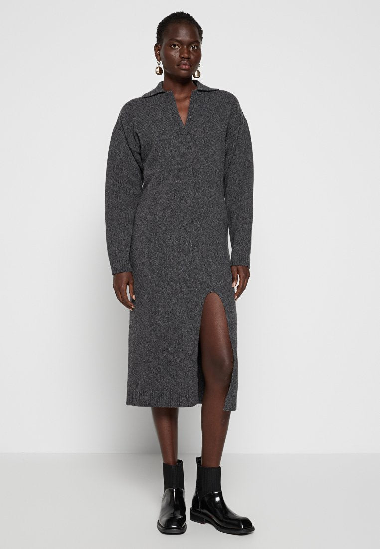 Graues gestricktes Kleid mit Kragen und langen Ärmeln, das einen schlitz bis zum Oberschenkel aufweist. Kombiniert mit schwarzen Knöchelstiefeln und strukturierten Strümpfen.