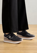 Schwarze und graue Sneaker mit einem glatten Lederobermaterial, einer erhöhten Sohle und einer weißen Zwischensohle, die ein Logo an der Seite und Schnürsenkel besitzen.
