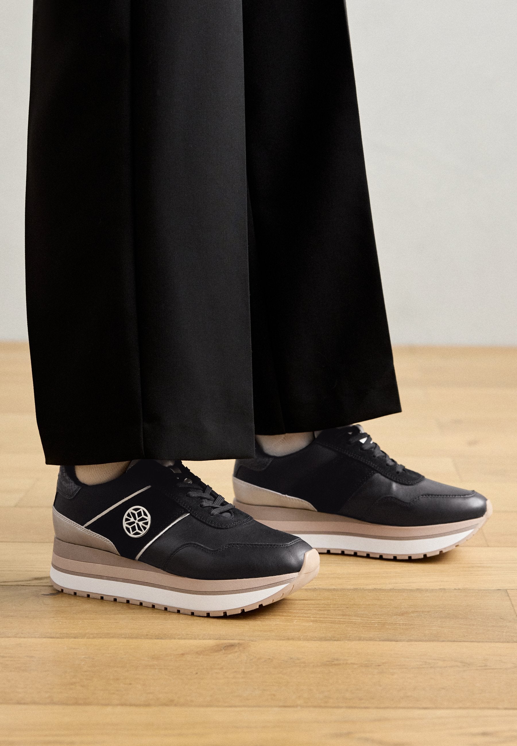 Schwarze und graue Sneaker mit einem glatten Lederobermaterial, einer erhöhten Sohle und einer weißen Zwischensohle, die ein Logo an der Seite und Schnürsenkel besitzen.
