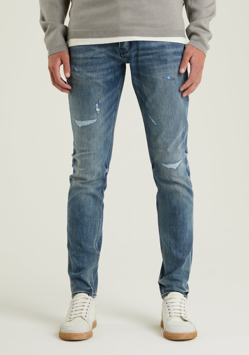 Dünne blaue Jeans mit einer mittleren Waschung und verwaschenen Details. Kombiniert mit weißen Turnschuhen, die einen lässigen Stil zeigen.