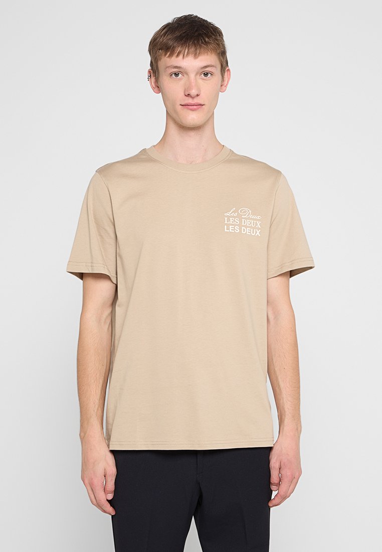 Beige Baumwoll-T-Shirt mit Rundhalsausschnitt und kurzen Ärmeln, mit dem weißen "Les Deux"-Logo auf der linken Brust.