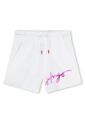 Weiße Baumwollshorts mit einem elastischen Bund, Kordelzugverschluss, zwei Seitentaschen und einem pinken reflektierenden "Hugo"-Logo auf der Vorderseite.