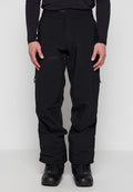 Mann trägt schwarze wasserdichte Hose mit Reißverschlusstaschen und schwarze Wanderschuhe, steht vor einem einfarbigen Hintergrund.
