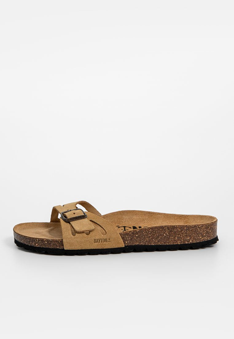 Hellbeige Wildledersandale mit einem einzigen Riemen und verstellbarem Metallverschluss. Kork-Mittelsohle und strukturierte schwarze Laufsohle, die ein leichtes Tragegefühl bietet.